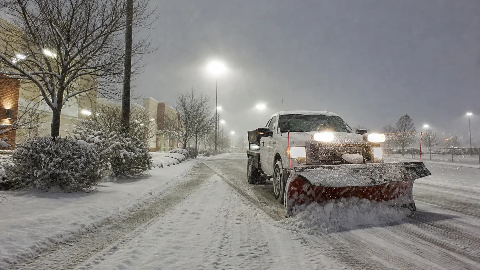 Commercial snow removal at a retail plaza during heavy snowfall.