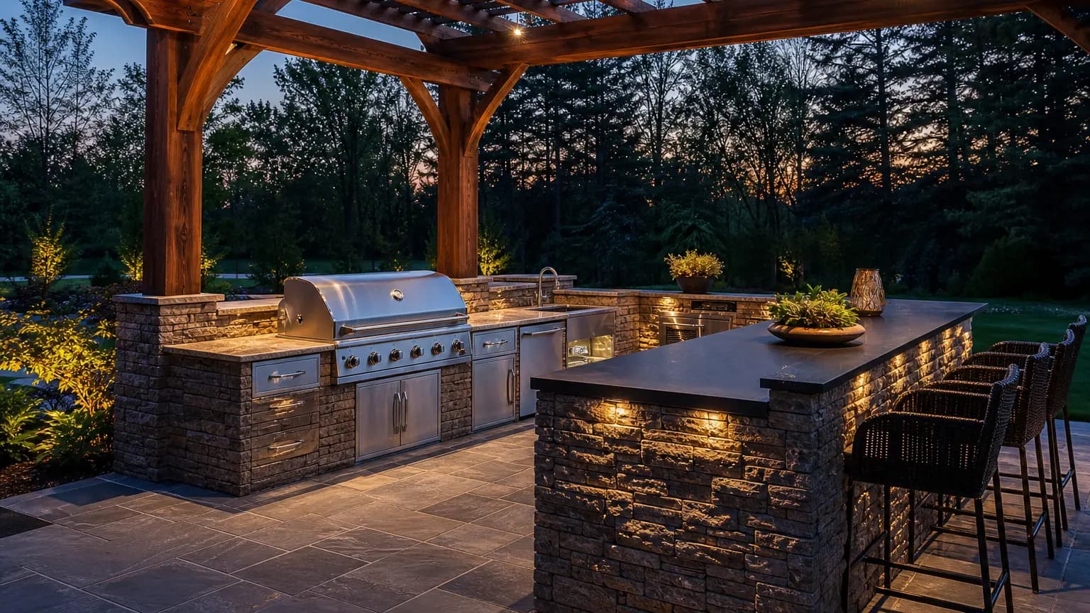 Built-in stone outdoor kitchen on a paver patio at dusk.
